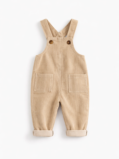 白背景のスタジオ撮影で、ベージュのコーデュロイ素材のベビー用オーバーオールが平置きで写っている。肩ストラップはボタン留めで、前面に大きなポケットが2つあり、裾はロールアップされている。
