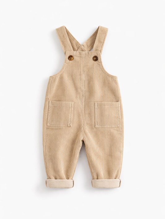 白背景のスタジオ撮影で、ベージュのコーデュロイ素材のベビー用オーバーオールが平置きで写っている。肩ストラップはボタン留めで、前面に大きなポケットが2つあり、裾はロールアップされている。

