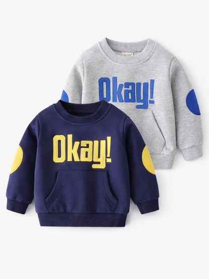 白背景の正面写真。子ども用スウェット2色セット：ネイビー（イエローの「Okay!」刺繍・フロントポケット・イエローヒジ当て）と、グレー（ブルーの「Okay!」刺繍・ブルーヒジ当て）。
