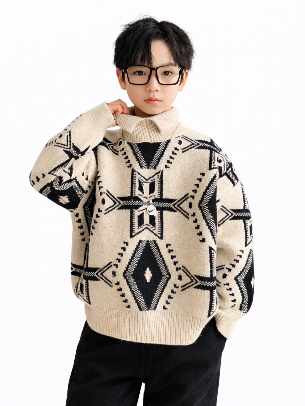 白背景のスタジオ写真。黒縁メガネの男の子モデルが、アイボリーのタートルネックニットを着用。黒の幾何学模様（クロス＆ダイヤ）デザインで、黒パンツと合わせたコーデ。
