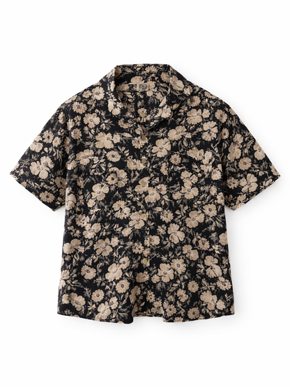 白背景の正面写真。ブラックベースにベージュの花柄プリントが入った半袖シャツ。開襟（オープンカラー）デザインで、フロントボタン留め。
