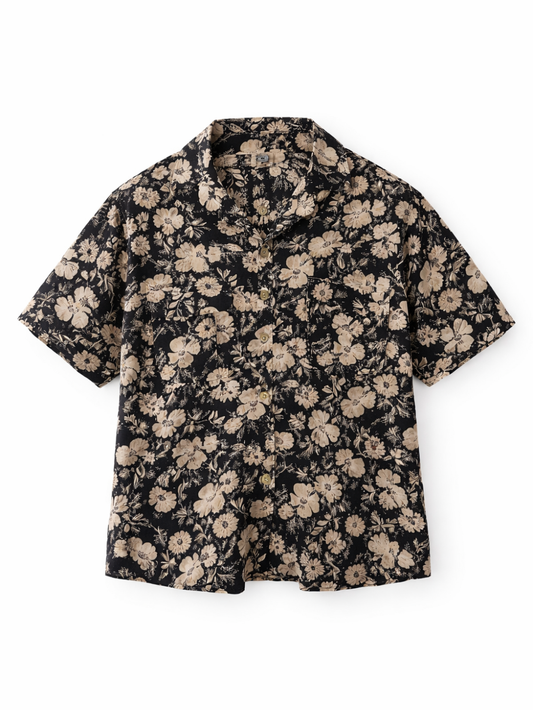 白背景の正面写真。ブラックベースにベージュの花柄プリントが入った半袖シャツ。開襟（オープンカラー）デザインで、フロントボタン留め。
