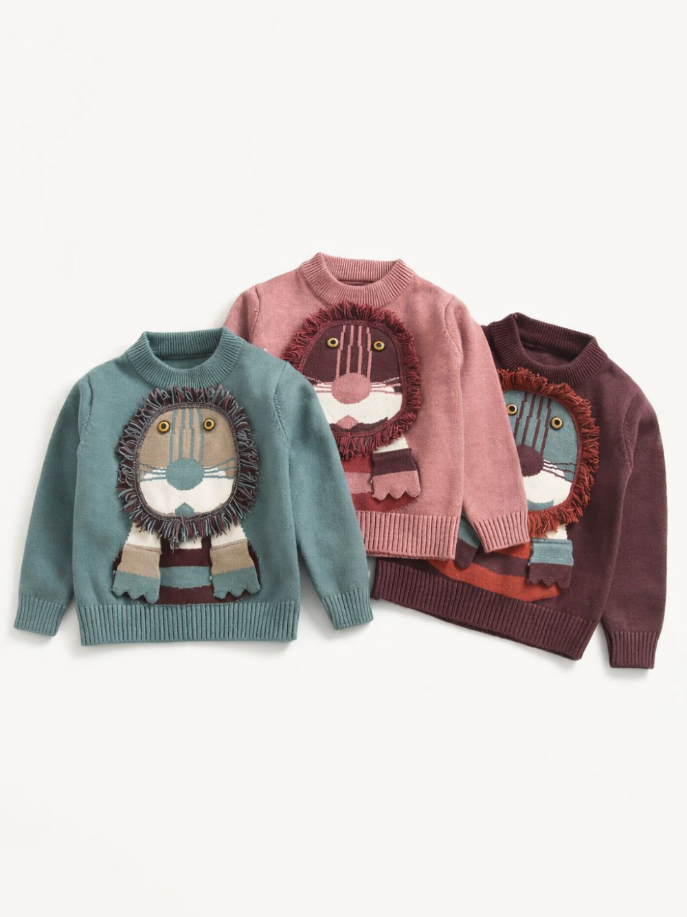 子ども用ライオンモチーフニットセーター3色（グリーン／ピンク／ブラウン）。立体フリンジのたてがみとマフラー風デザインが特徴の長袖プルオーバー。
