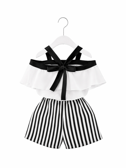 ガールズ用2点セット。ホワイトのオフショルダーフリルトップスにブラックのストラップ＆リボン付き。ボトムはブラック×ホワイトの縦ストライプショートパンツ（ウエストゴム）。ハンガー掛け、白背景の商品画像。
