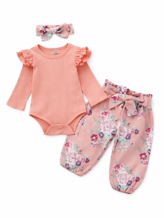 ベビー女の子用3点セット。ピーチピンクのリブ長袖ロンパース（肩フリル付き）、ピンクベースの花柄パンツ（ウエストリボン付き）、同柄のリボンヘアバンドの組み合わせ。白背景の商品画像。
