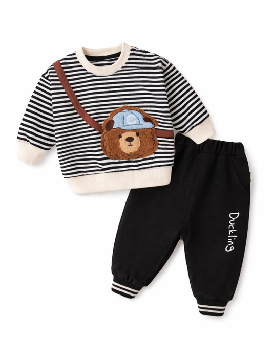 白いスタジオ背景で撮影した、ベビー／キッズ用2点セット。黒白ボーダーの長袖トップスに、斜め掛けストラップ風デザインとクマのアップリケ（帽子付き）が付いている。ボトムは黒のジョガーパンツで、脚に「Duckling」ロゴプリント。セット全体が見えるカタログ写真。
