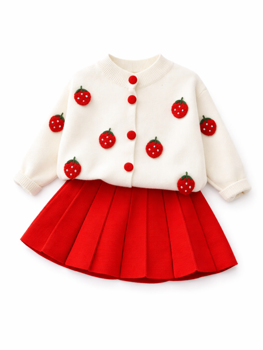 白いスタジオ背景で撮影した、女の子用ニットセットアップ。アイボリーのカーディガンは赤いボタンといちごモチーフの刺繍が散りばめられ、ボトムは鮮やかな赤のプリーツニットスカート。上下セットがはっきり見えるカタログ写真。
