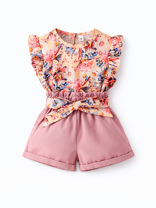 白いスタジオ背景で撮影した、女の子用サマーセットアップ。フリル袖の花柄トップス（ピーチ系ベースにカラフルなフローラルプリント）と、くすみピンクのハイウエストショートパンツの2点セット。ウエストに同柄の大きなリボンベルト付きで、全体が見えるカタログ写真。
