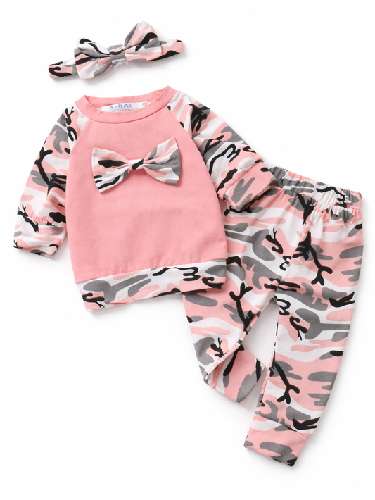女の子ベビー用3点セット（ピンク長袖トップス・迷彩柄パンツ・リボンヘアバンド）の商品画像。ホワイト背景のスタジオ撮影で、トップスは胸元にリボン付き、袖と裾はピンク・グレー・ブラックの迷彩柄、同柄のロングパンツとヘアバンドがセットになっています。