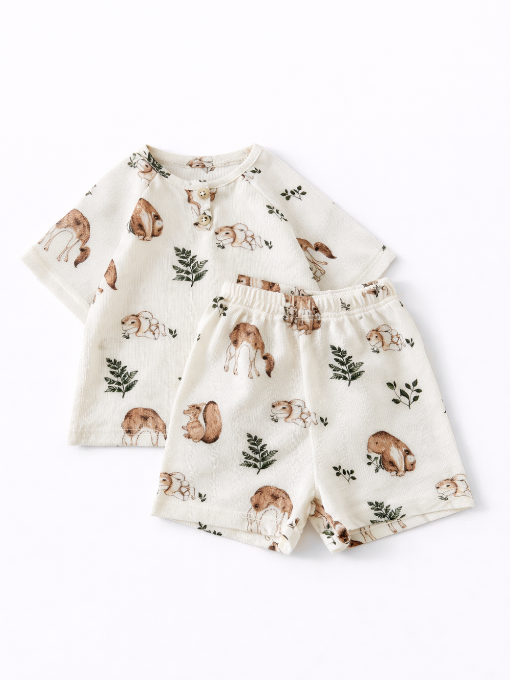 白背景に置かれた、森の動物と植物柄のクリーム色キッズ上下セット（半袖トップス＋ショートパンツ）の商品写真
