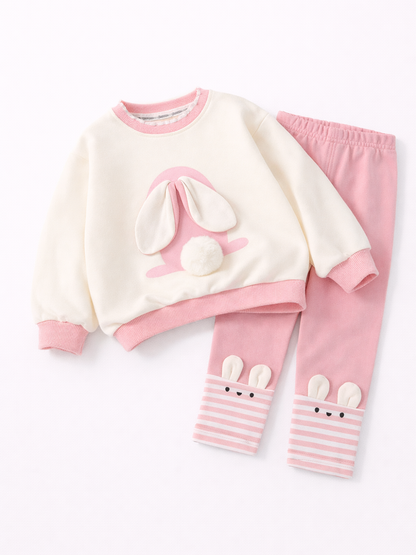白背景に配置された子ども用上下セット。アイボリーの長袖トレーナーに立体うさぎ耳としっぽのモチーフ、ピンクのパンツは裾にボーダー柄とうさぎ顔デザイン入りの可愛い2点セット。