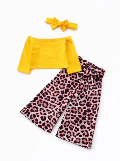 白背景に、キッズ用の2点セット（イエローのオフショルダー長袖トップス＋レオパード柄のワイドパンツ）と、同色のリボンヘアバンドが並べて置かれている商品写真。

