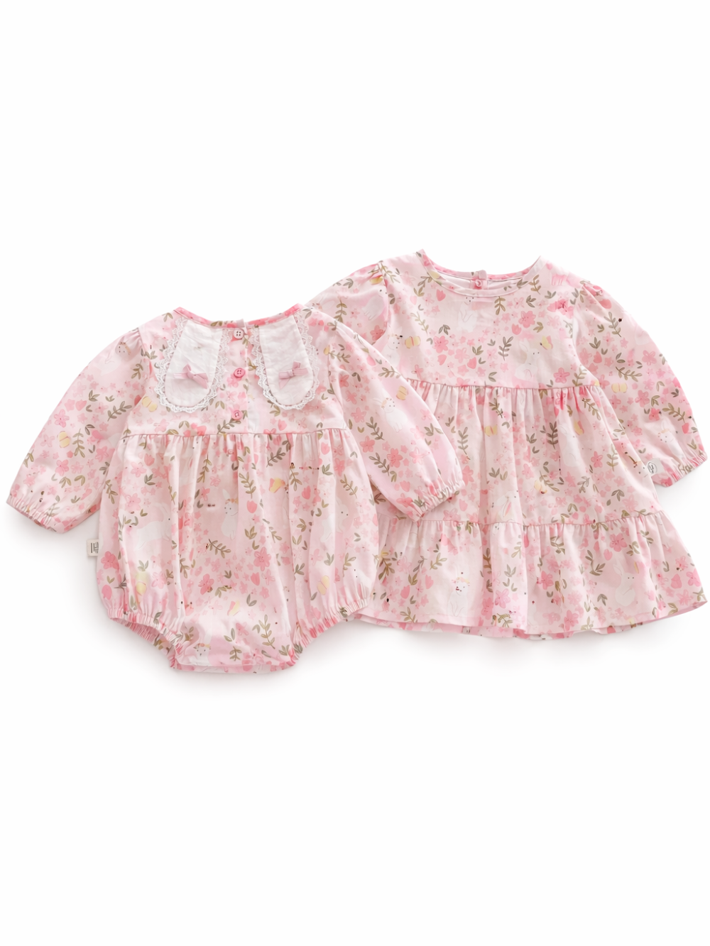 ピンクの花柄ベビーウェア2点セットの商品画像。左はレース襟付きの長袖ロンパース、右はティアードデザインの長袖ワンピースで、やわらかな総柄プリントが入ったコットン風生地のキッズ服セット。