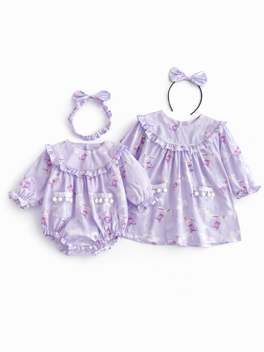 ラベンダーカラーのベビーウェア2点セットの商品画像。左は長袖ロンパース、右は長袖ワンピースで、うさぎ柄プリントとフリルヨーク、ポンポン付きポケットが特徴のキッズ服セット。