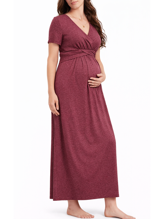 白背景のマタニティワンピース着用イメージ。日本人妊婦モデルが、ワインレッドのVネック半袖ロングワンピース（胸下切替・クロスデザイン）を着用し、お腹に手を添えて立ち姿でシルエットを見せている。
