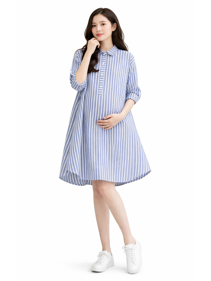 白背景のマタニティワンピース着用イメージ。日本人妊婦モデルが、ブルー×ホワイトのストライプ柄シャツワンピース（襟付き・前立てボタン・七分袖・Aライン・後ろ下がりの裾）を着用し、お腹に手を添えてカタログ風ポーズで立っている。