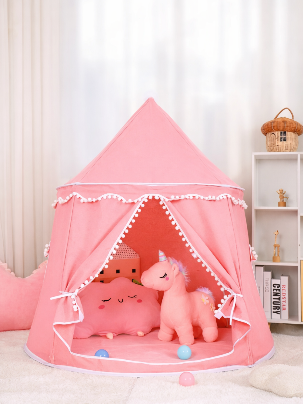テキストのない室内で、白いラグの上にピンクの城型キッズテントが置かれ、入口には白いポンポン飾りが付き、テント内にピンクの雲形クッションとユニコーンのぬいぐるみ、小さなボールが見える。