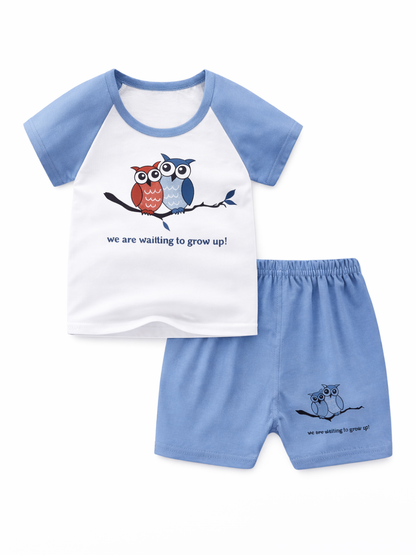 白背景のスタジオ撮影。ライトブルーのラグラン袖と同色ショートパンツのキッズ2点セット。白いTシャツ前面に2羽のフクロウのイラストと英字メッセージがプリントされ、ショートパンツの裾にもフクロウ柄と英字プリントが入っている。
