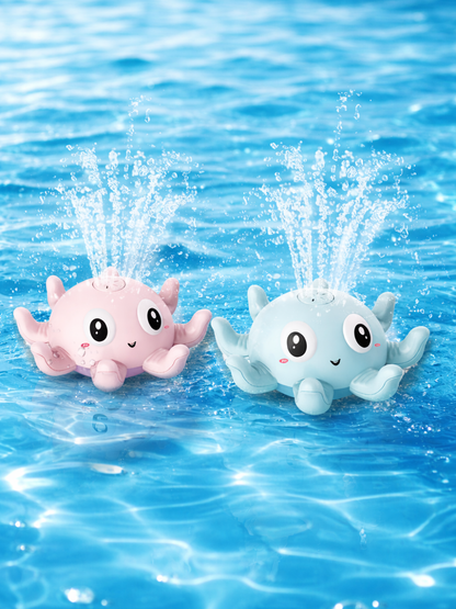 青く澄んだ水面に浮かぶタコ型の噴水バストイ2個。パステルピンクとライトブルーの本体に大きな目と笑顔があり、頭頂部から水が噴き上がって水しぶきと小さな泡が広がっている。
