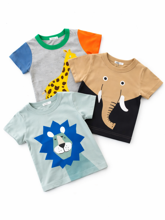 白背景のフラットレイで重ねて配置されたキッズ半袖Tシャツ3枚。グレー地にキリン柄（グリーン襟・ブルーとオレンジの袖）、ベージュ×ブラック配色にゾウの顔プリント、ライトブルー地に青いたてがみのライオンプリントが描かれている。
