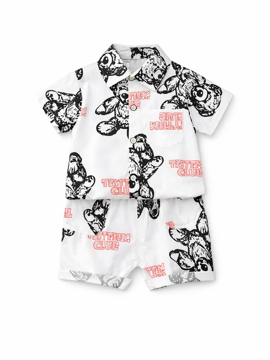 白背景のスタジオ撮影。子ども用の半袖シャツとショートパンツの2点セットが単体で配置されている。白地に黒のテディベア線画プリントと赤い「SYSTEM CLUB」文字デザイン入りで、シャツはボタン留めと胸ポケット付き、パンツは同柄のショート丈。
