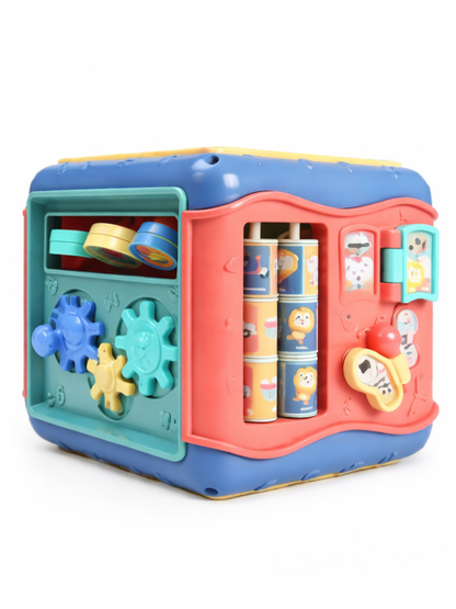白背景で、幼児向けの知育アクティビティキューブを斜めから撮影した商品画像。ブルー×コーラル×グリーンの本体に、歯車パーツ、回転ドラム、リング遊びなどの仕掛けが付いている。
