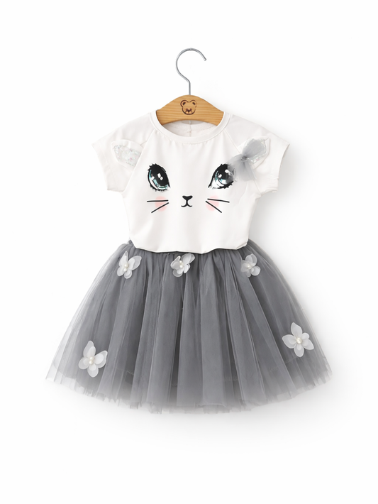 女の子用ワンピース。白い半袖トップスに猫の顔プリント（大きな目・ひげ・ほほ色）と肩のリボン付き。グレーのチュールスカートは立体の花飾り付き。ハンガーに掛けた状態で白背景。
