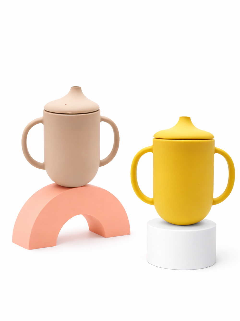 ベージュとイエローのシリコン製ストローマグ2個。両側ハンドルとこぼれにくいフタ付きで、白背景に並べて配置されている。
