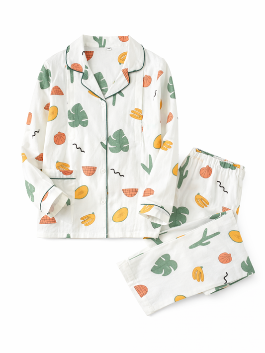 白地にボタニカル柄（グリーンの葉・オレンジ系モチーフ）の長袖パジャマ上下セット。襟付き前開きシャツにグリーンのパイピングとボタン付きで、同柄のロングパンツ（ウエストゴム）がセット。白背景で単品。
