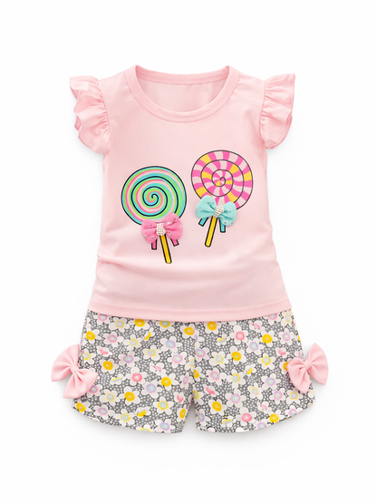 ピンクのフリル袖Tシャツと花柄ショートパンツの女の子用2点セット。トップスはカラフルなキャンディ（ロリポップ）プリントとリボン飾り付きで、パンツは両サイドにピンクのリボンが付いている。白背景で単品。
