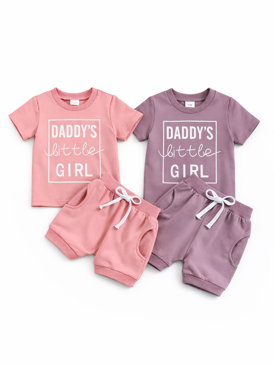 白背景に、ベビー用の半袖Tシャツ＆ショートパンツ2色セット（ピンク／モーブ）を並べた商品画像。各Tシャツは「DADDY’S little GIRL」プリント入りで、パンツは白いドローストリング付き。
