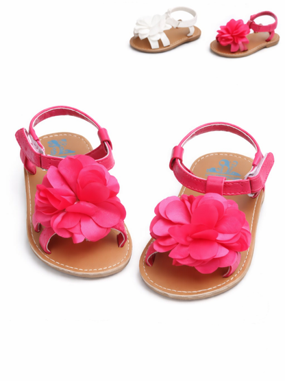 ピンクの大きなフラワー飾り付きベビーサンダル（左右1足ずつ）を白背景に並べた商品写真。上部にホワイトとピンクの別カラーサンダルが小さく写っている。
