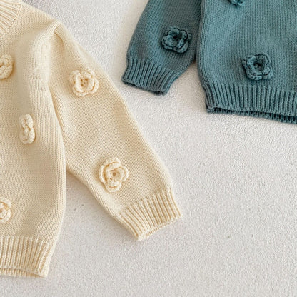 ナチュラルなラグの上に並べたアプリコット色の花柄ベビーニットのライフスタイル画像  
