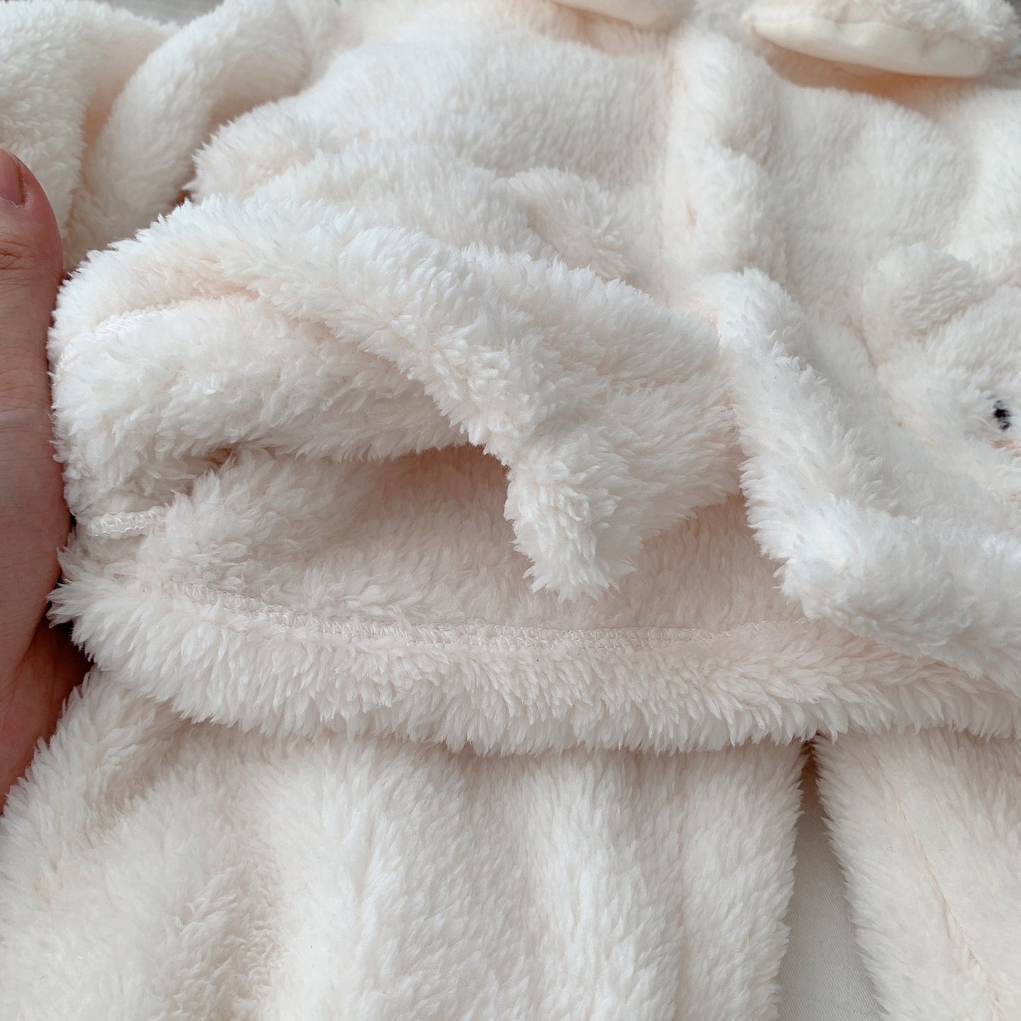ふわふわしたホワイトボア生地の端を指でつまんだ子ども用くま刺繍ボア上下セットの質感クローズアップ
