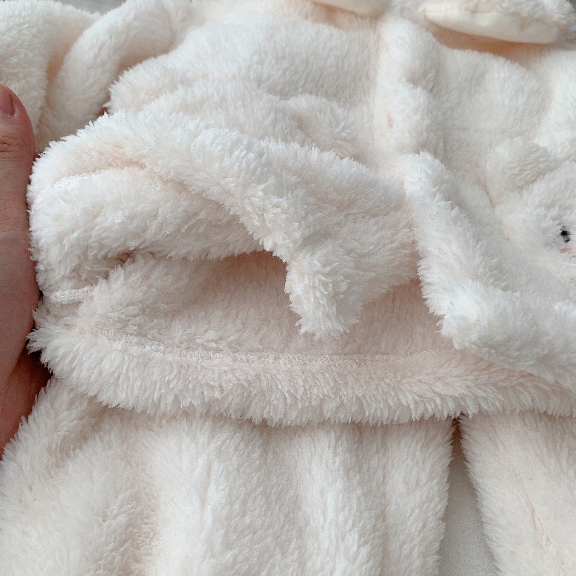 ふわふわしたホワイトボア生地の端を指でつまんだ子ども用くま刺繍ボア上下セットの質感クローズアップ
