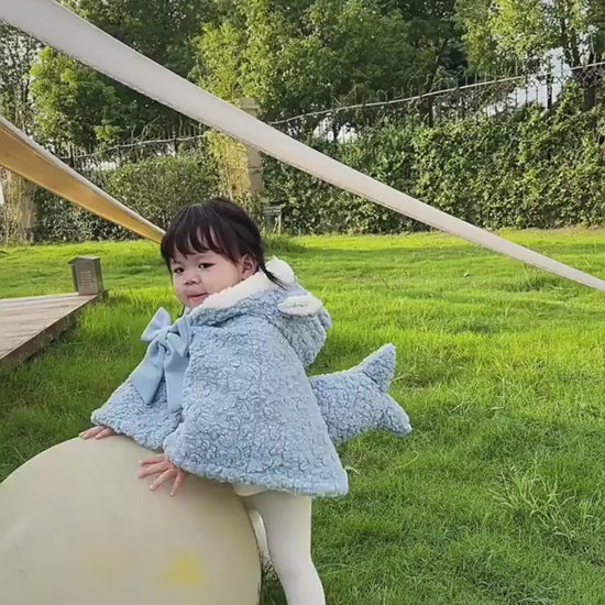 芝生の上で子どもがライトブルーのサメモチーフケープを羽織っている着用イメージ
