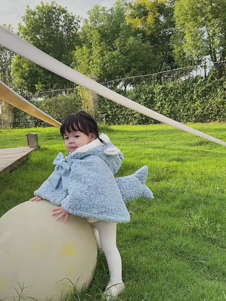 芝生の上で子どもがライトブルーのサメモチーフケープを羽織っている着用イメージ
